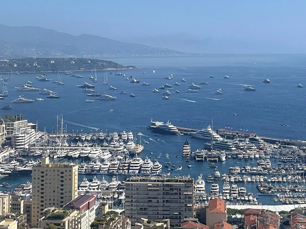 Aerial view of Port Hercule during Monaco Yacht Show week — dozens of superyachts moored inside the harbour and anchored in the bay stretching toward Cap Martin in the distance