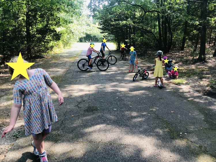 Children walk, sit, and ride bikes and scooters on a path at Bare Cove.
