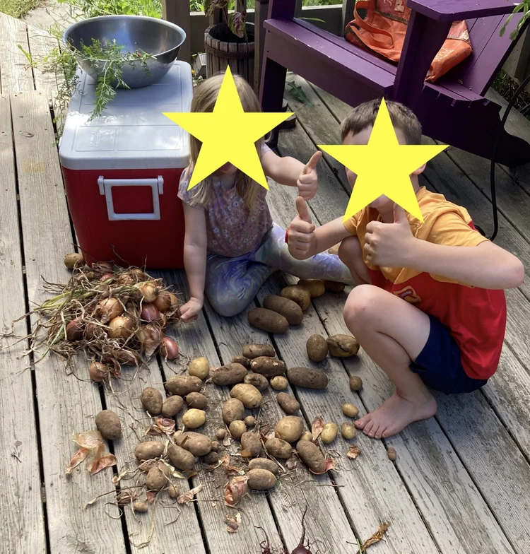 Two children sit over their potato harvest, giving "thumbs up".