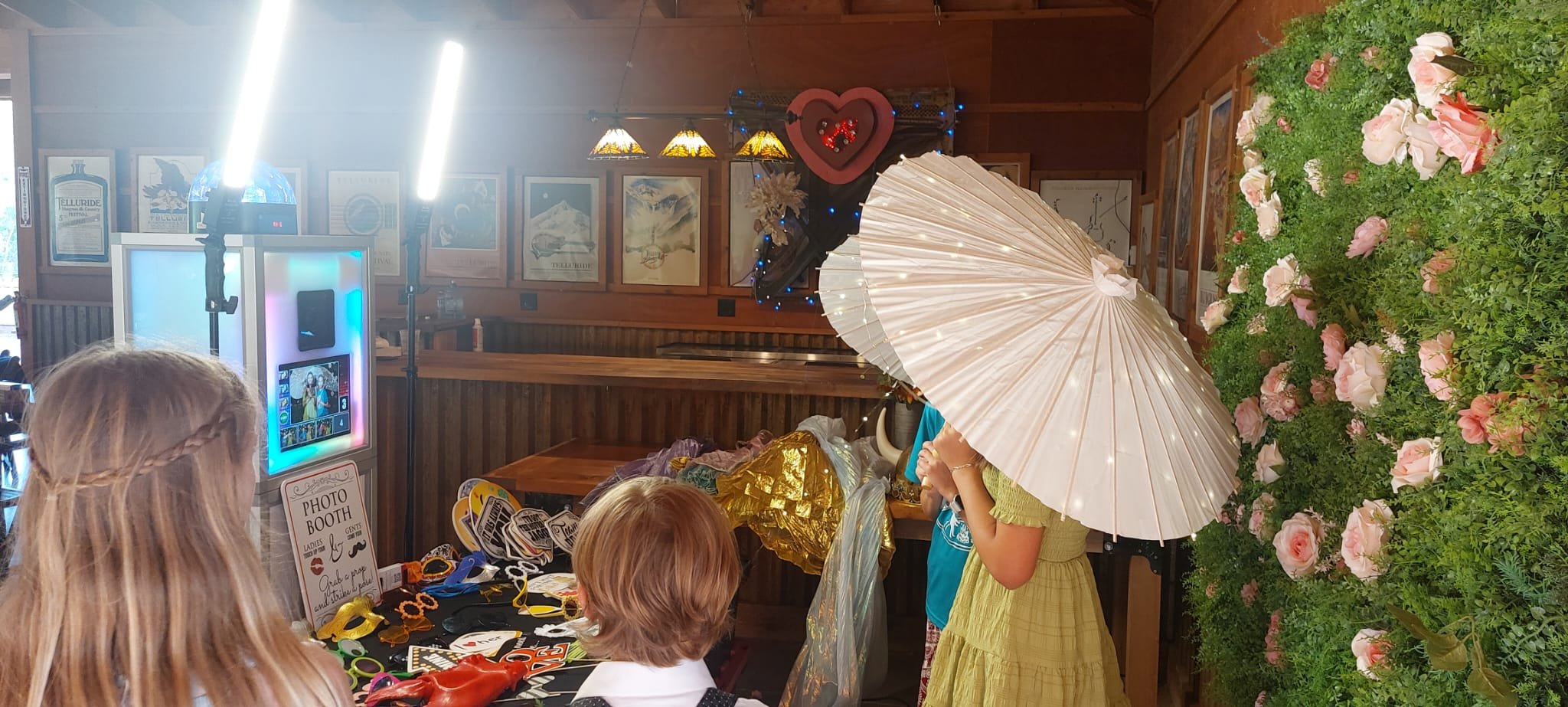 Guests at a 303 Photo Booth with a prop table, parasols and a flower wall