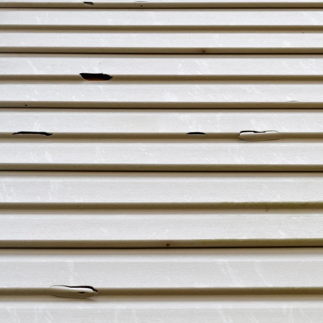 hail-damaged vinyl siding with hidden crack near window