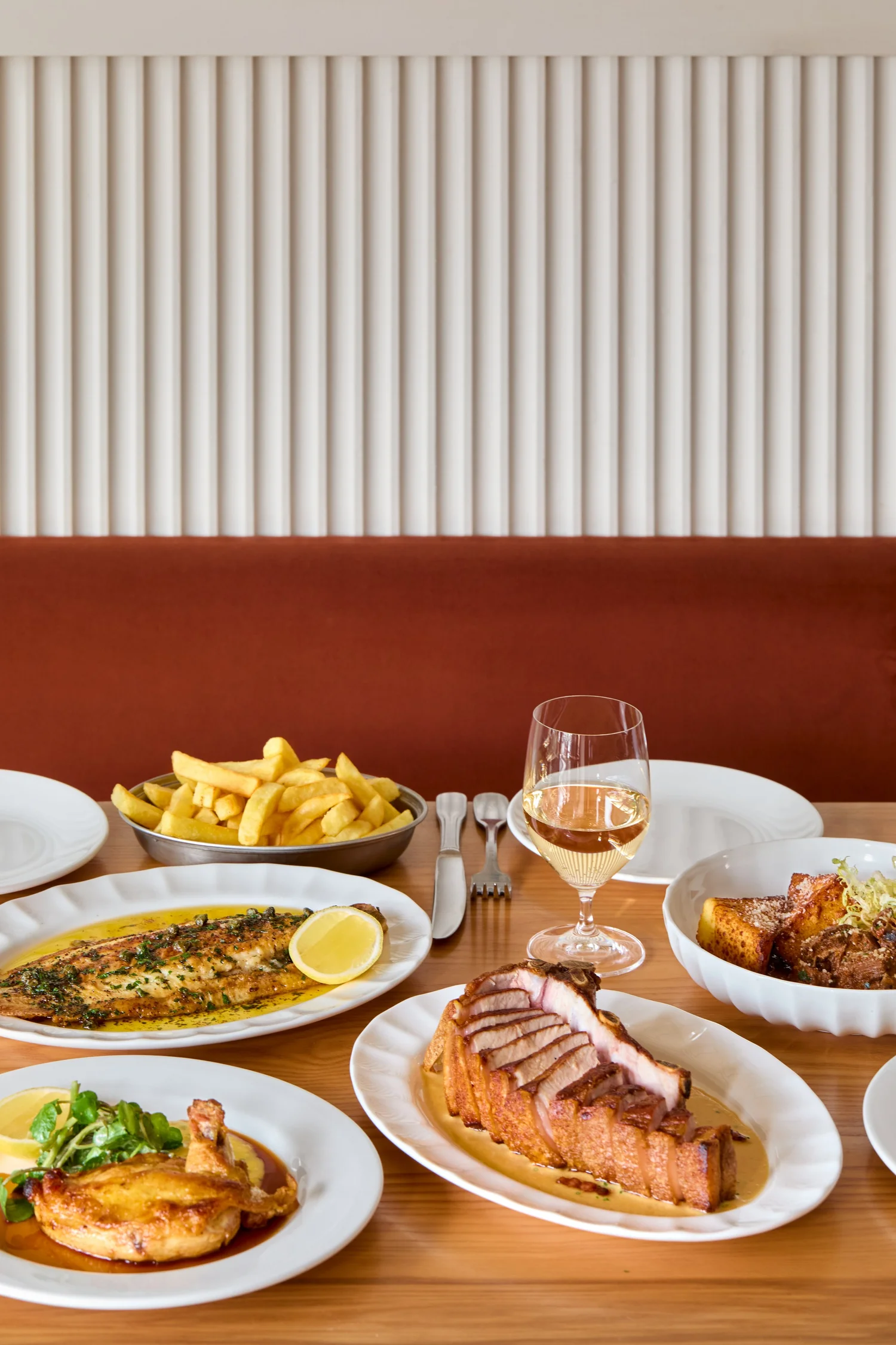 Dover sole, pork chop, chips and wine on a table at Gina