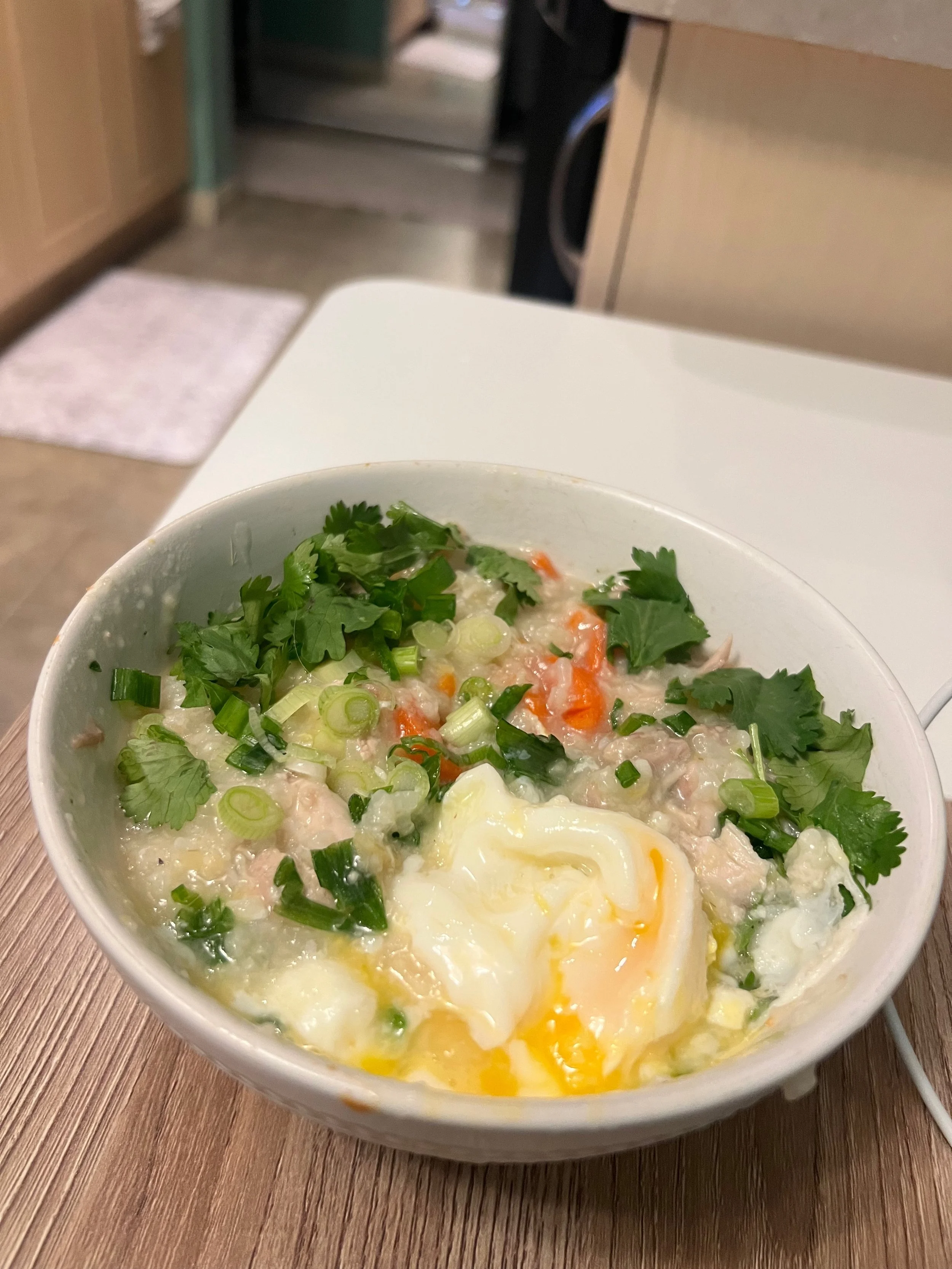 A warm bowl of ginger chicken congee garnished with fresh scallions, cilantro, and a soft poached egg