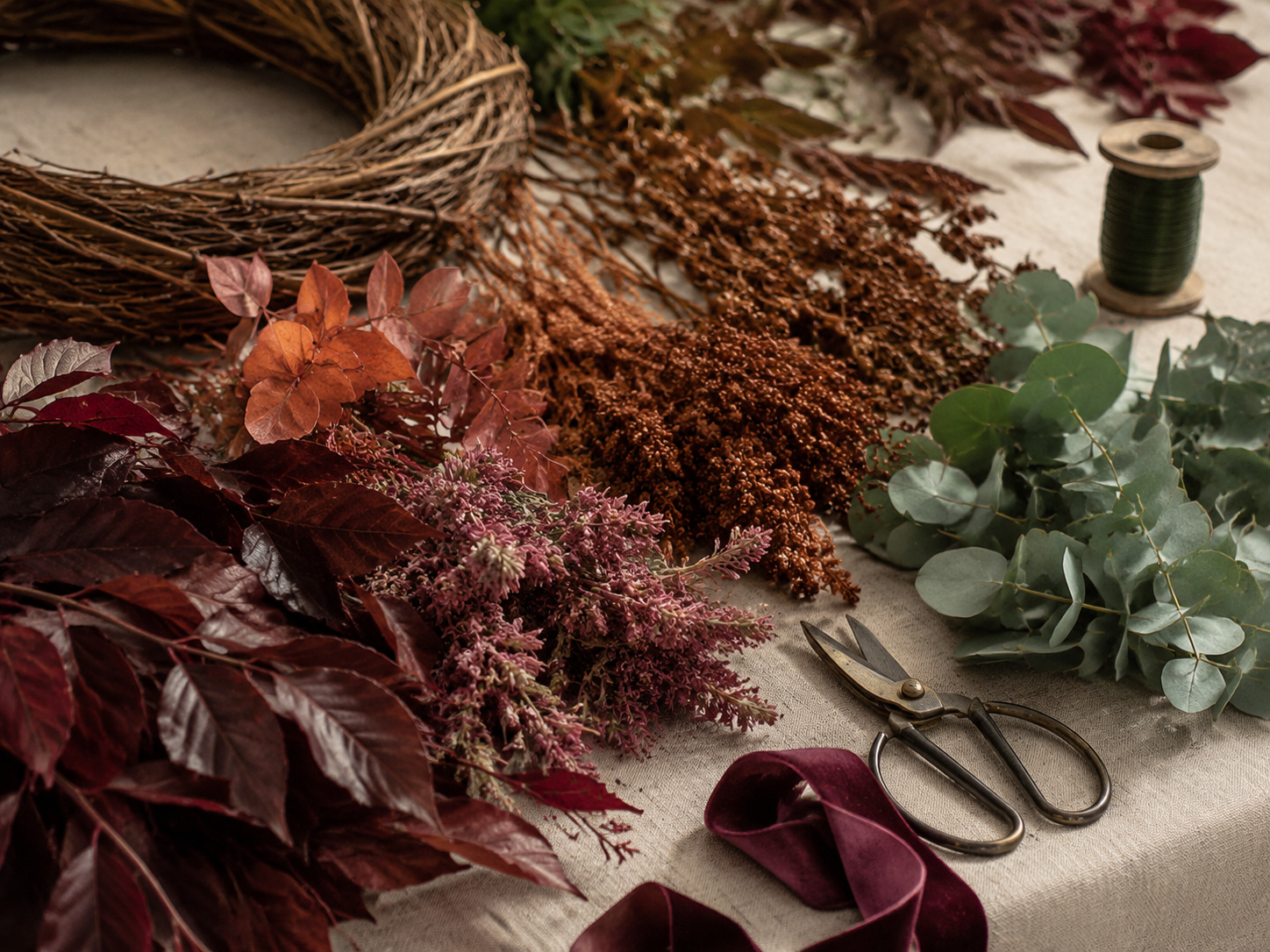 Fall wreath-making supplies with burgundy foliage, eucalyptus, ribbon, wire, and floral snips