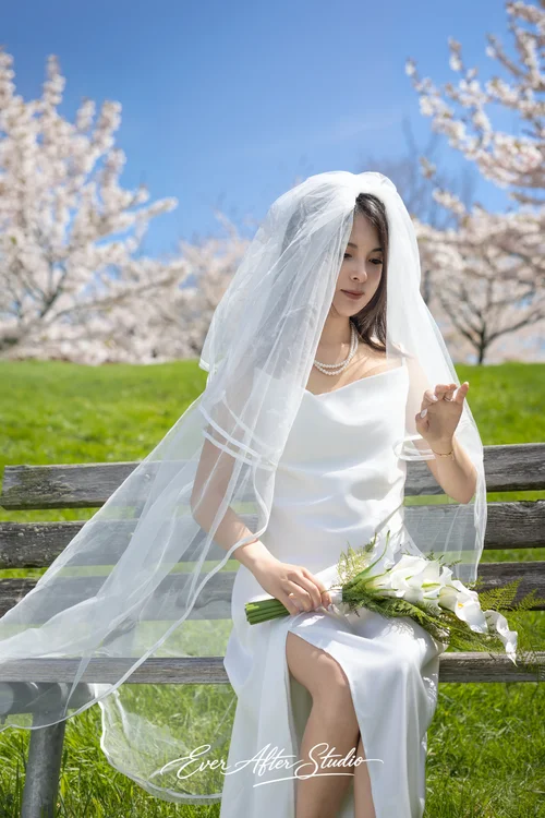Woman in a white dress and veil holding flowers on a sunny lawn