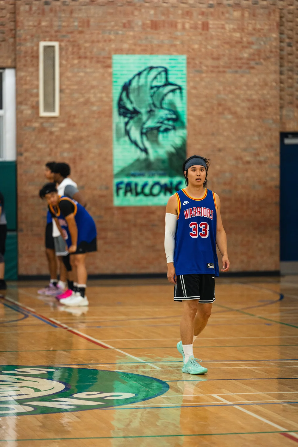 Warriors number 33 stands on the court in front of a brick wall and Falcons mural.