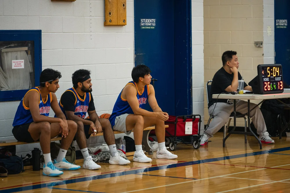 Three Warriors players sit on a bench beside the scorer’s table.