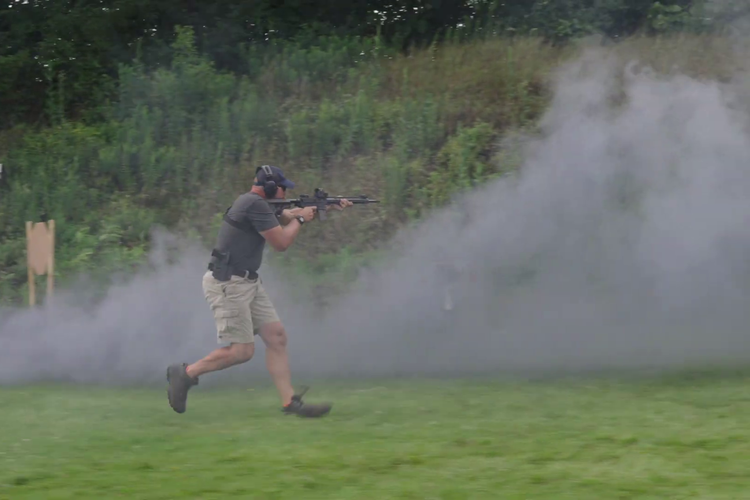 A person carrying a rifle running beside a cloud of smoke