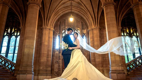 Couple embracing beneath stone arches with a veil stretched into the light