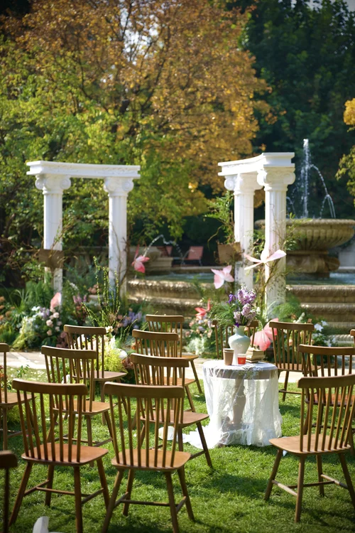 Rows of gold chairs and flowers leading to white columns in a garden