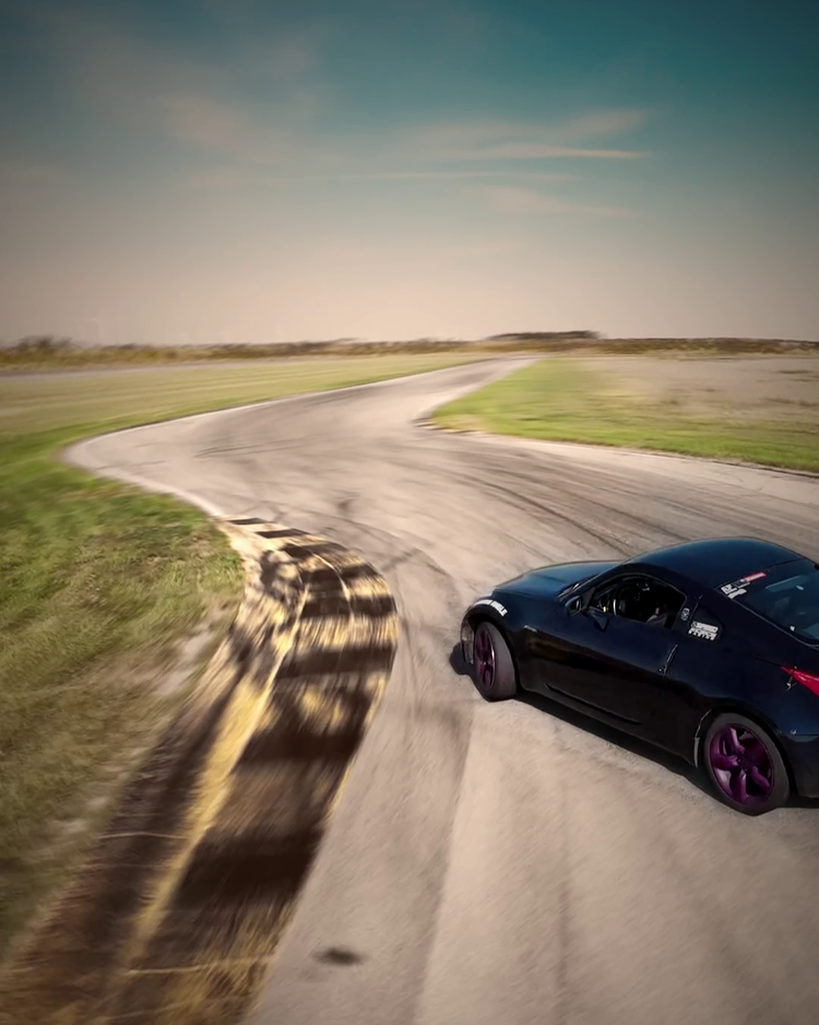 A dark drift car rounding a sunlit bend on a racetrack
