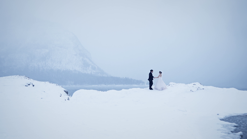Two figures crossing a snowy landscape beneath misty mountains