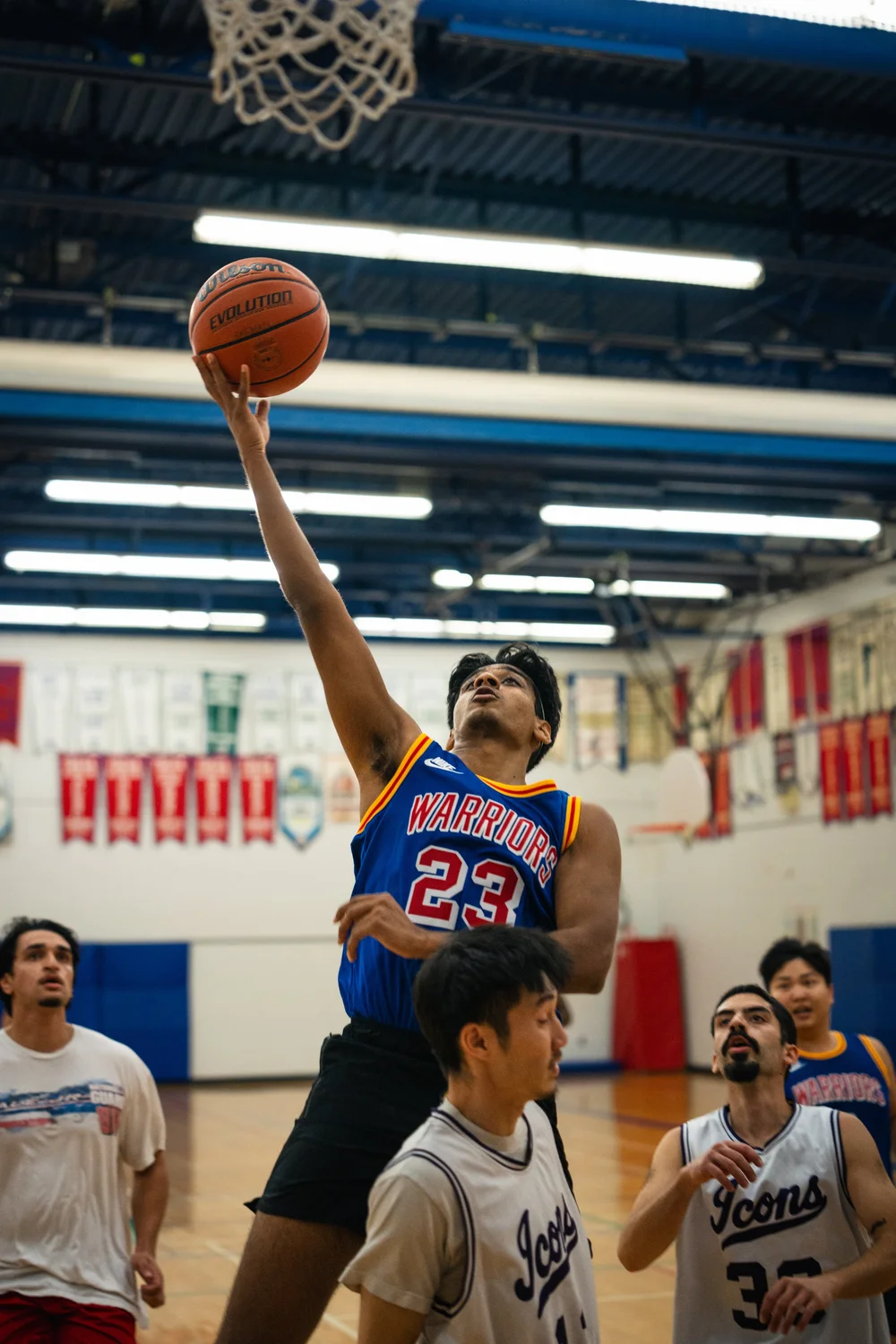 Warriors number 23 extends the ball toward the hoop above surrounding white-shirted players.