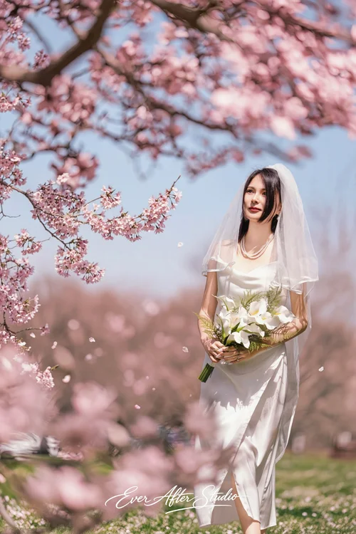 Woman holding a white bouquet beneath pink flowering branches