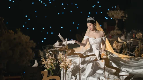 Woman in a white gown seated at a flower-filled table beneath blue lights