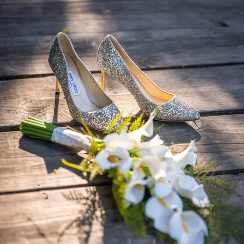 Embellished shoes and a white bouquet on a wooden surface