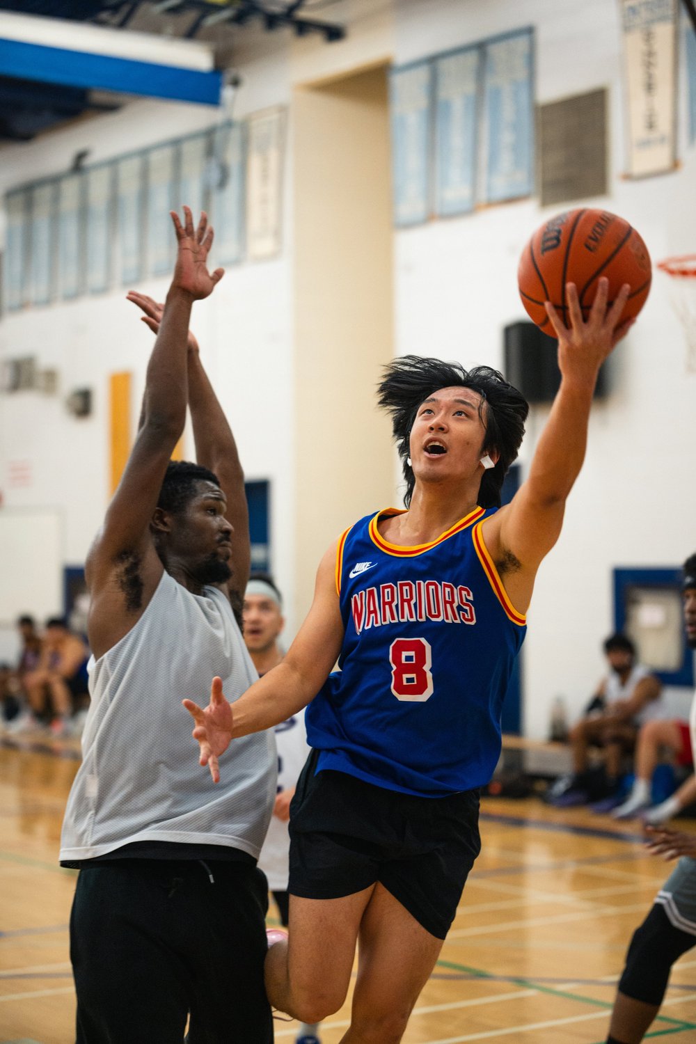 Warriors number 8 holds the ball high in one hand beside a white-shirted defender with raised arms.