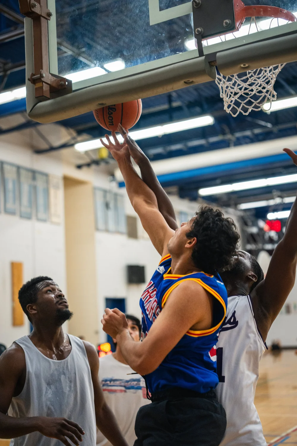 A Warriors player and a white-shirted defender reach for the ball beneath the backboard.