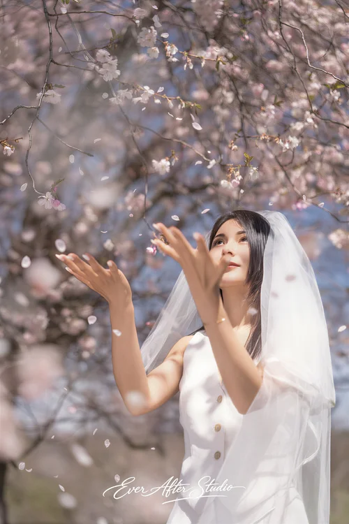Veiled woman lifting her hands toward pale pink blossoms