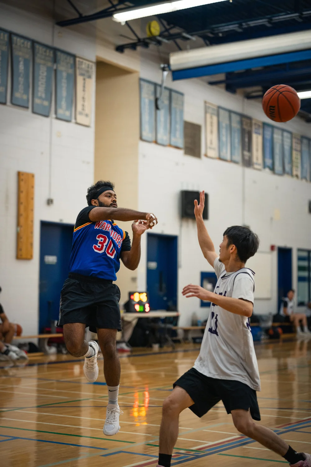 Warriors number 30 releases the ball in the air as a white-shirted defender raises an arm.
