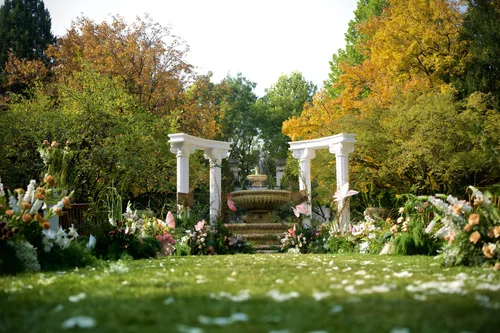 Outdoor ceremony chairs facing a flower-lined aisle and white columns