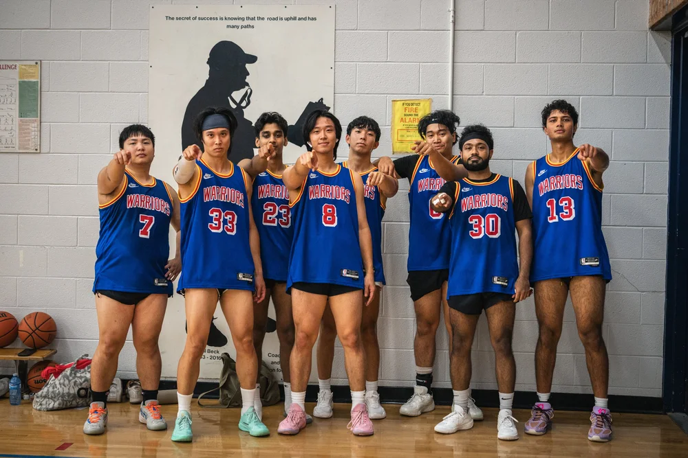 Eight Warriors players in blue point toward the camera against the gym wall.
