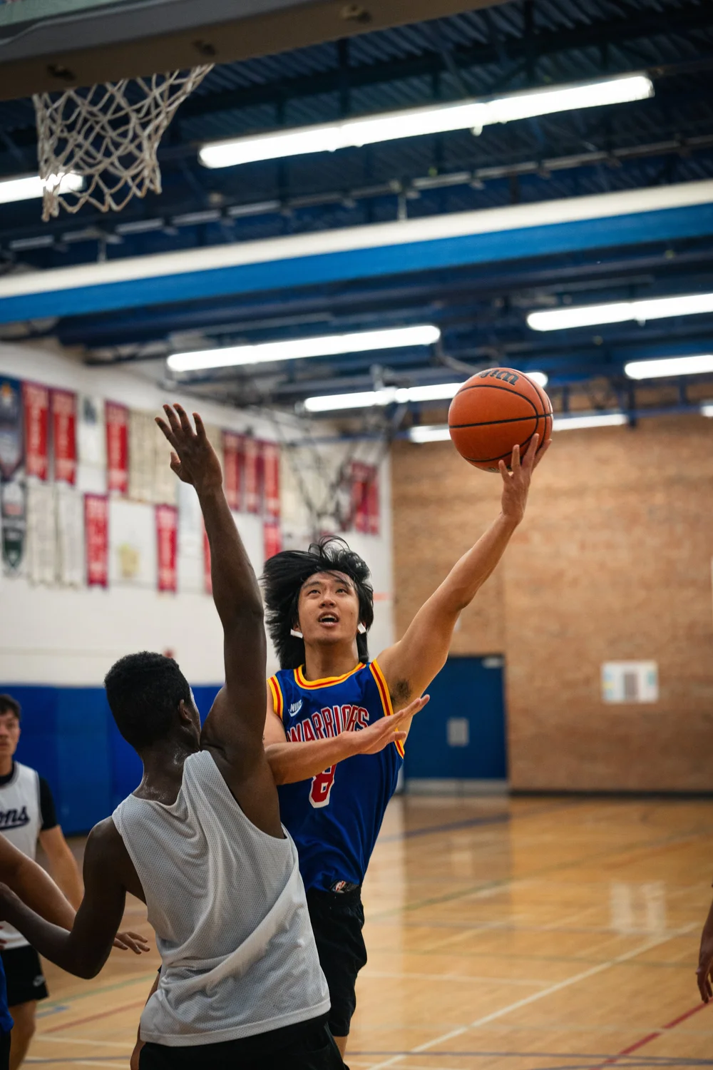 Warriors number 8 reaches up with the basketball as an unnumbered white-shirted defender contests.