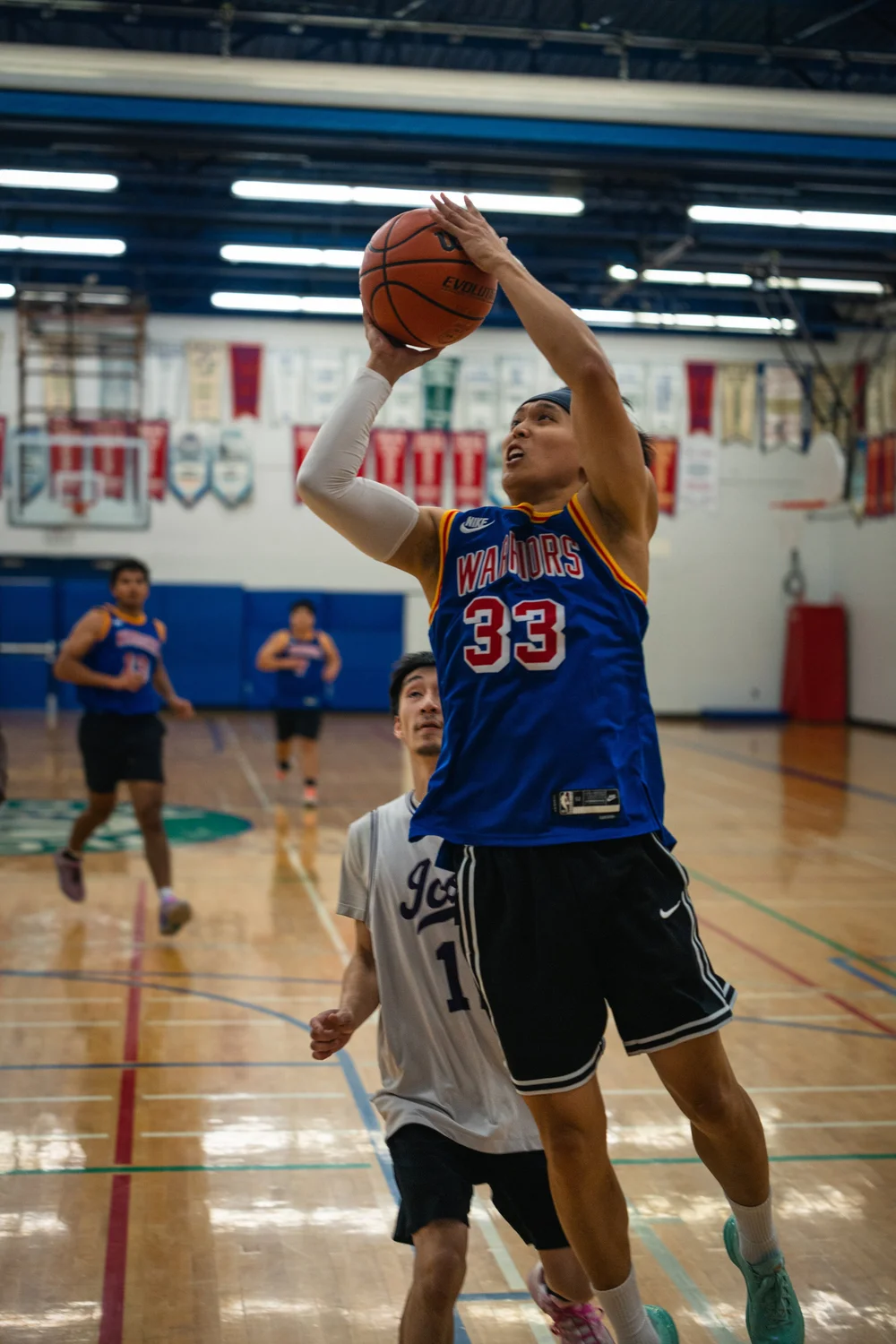 Warriors number 33 rises with both hands on the ball while a white-shirted defender trails.