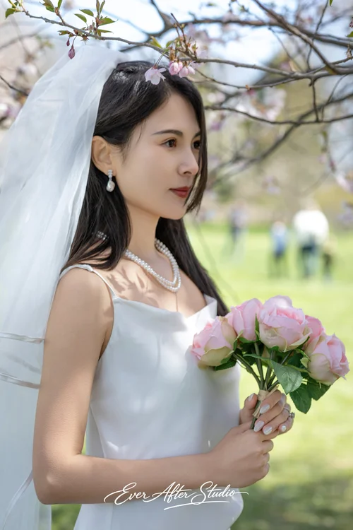 Close portrait of a veiled woman holding a pink bouquet in a sunlit park