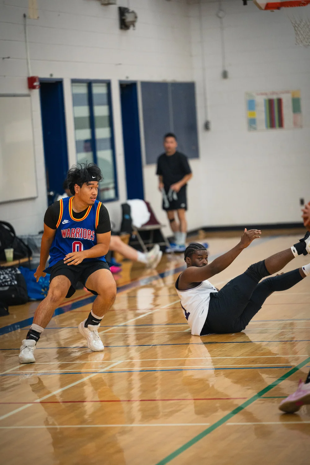 Warriors number 0 turns beside a white-shirted player with raised legs on the floor.