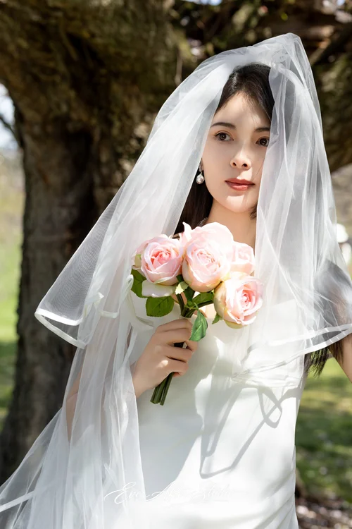Close portrait of a veiled woman holding pink roses beside a tree