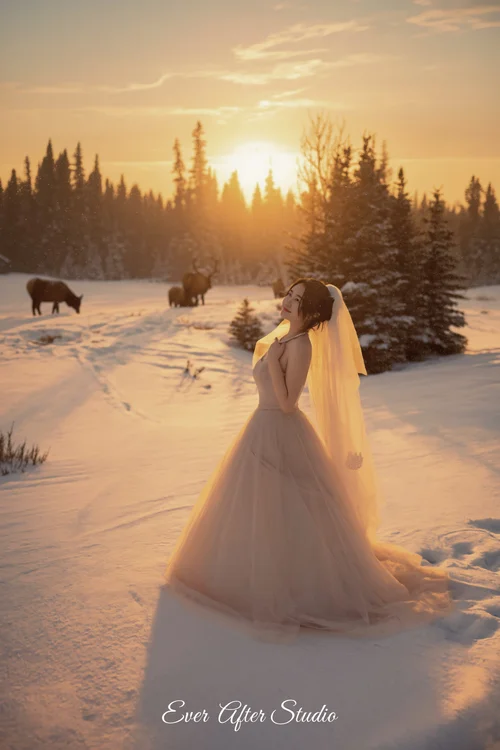 Woman in a white gown in a snowy clearing at sunset