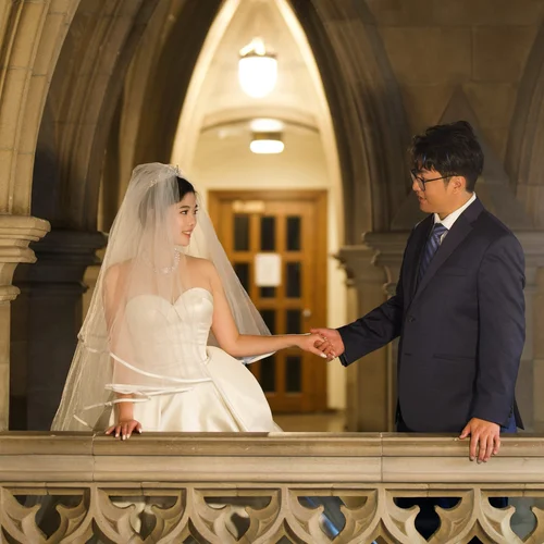 Couple holding hands across a stone balustrade beneath an arch
