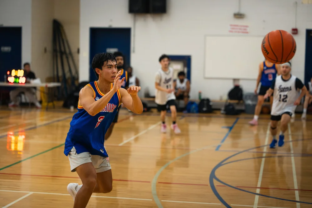 A blue-shirted Warriors player follows through on a pass with the ball high at the right.