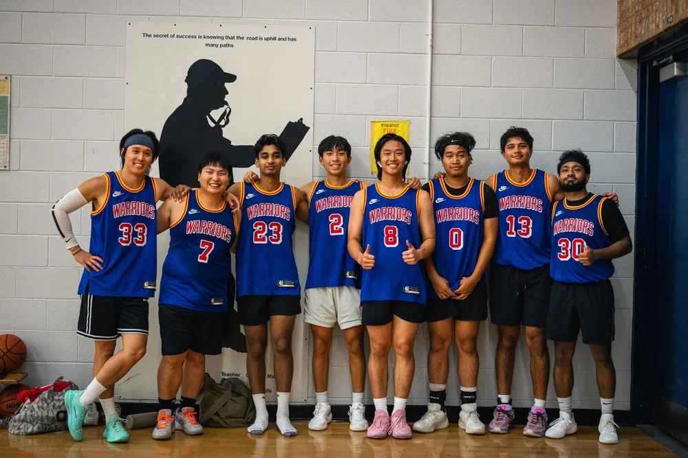 Eight Warriors players in blue pose shoulder to shoulder against the gym wall.