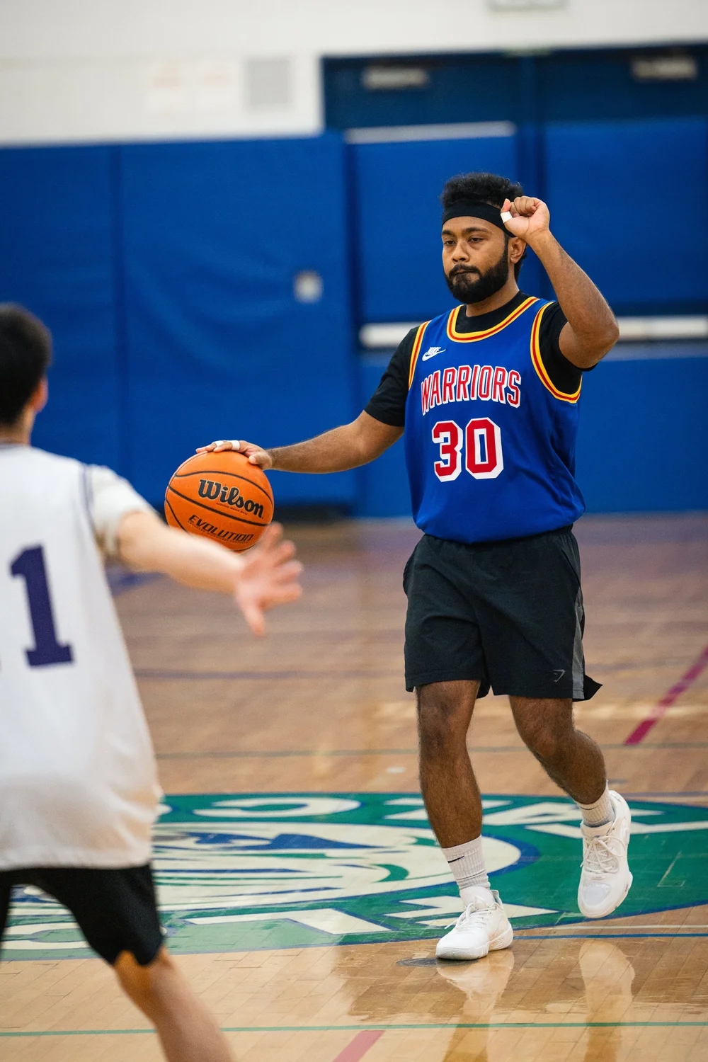 Warriors number 30 holds a basketball and raises a hand as a white-shirted defender approaches.