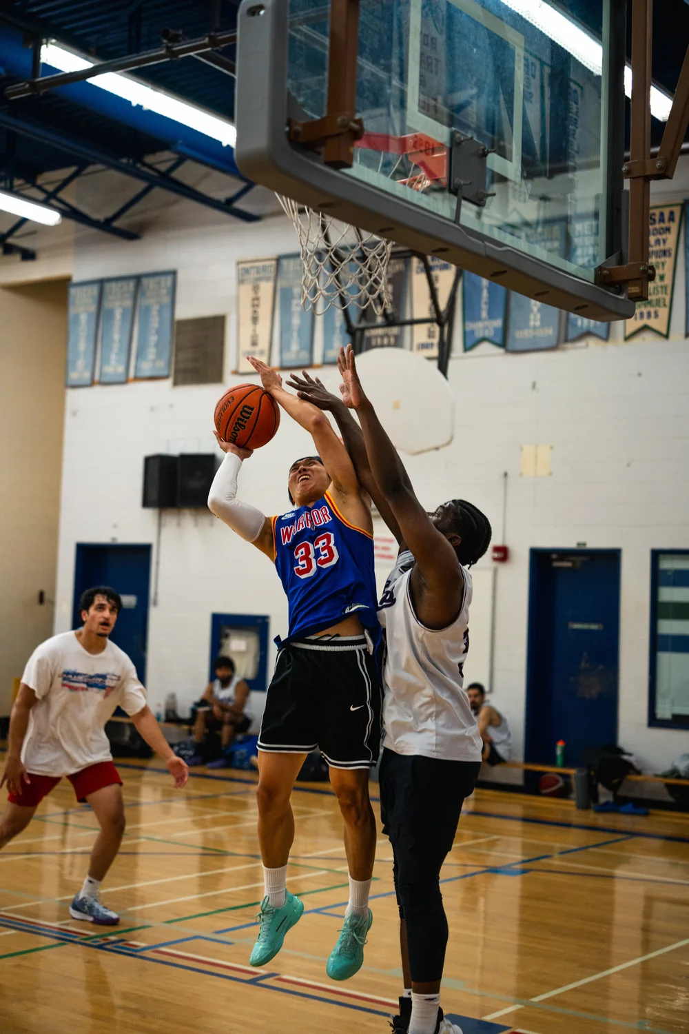 Warriors number 33 holds the ball high while a white-shirted defender contests under the hoop.