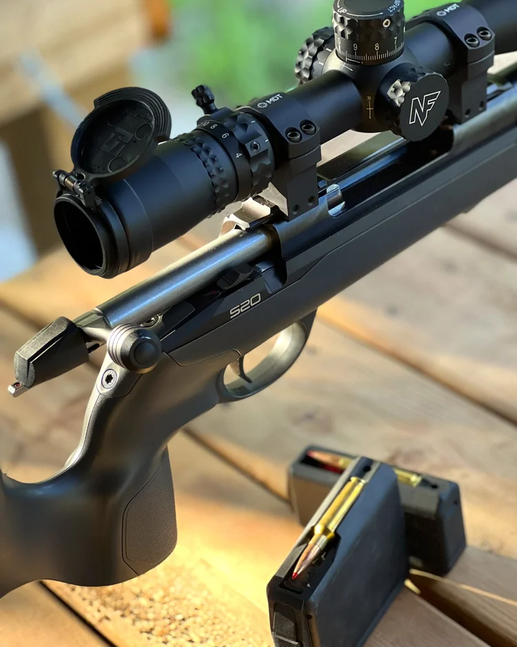 Close view of a scoped rifle and magazines on a wooden table