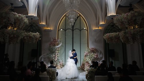 Couple beneath a vaulted arch surrounded by flowers and seated guests
