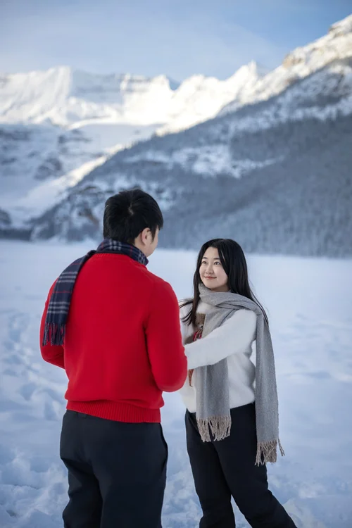 Couple in winter clothing facing each other in a snowy mountain landscape