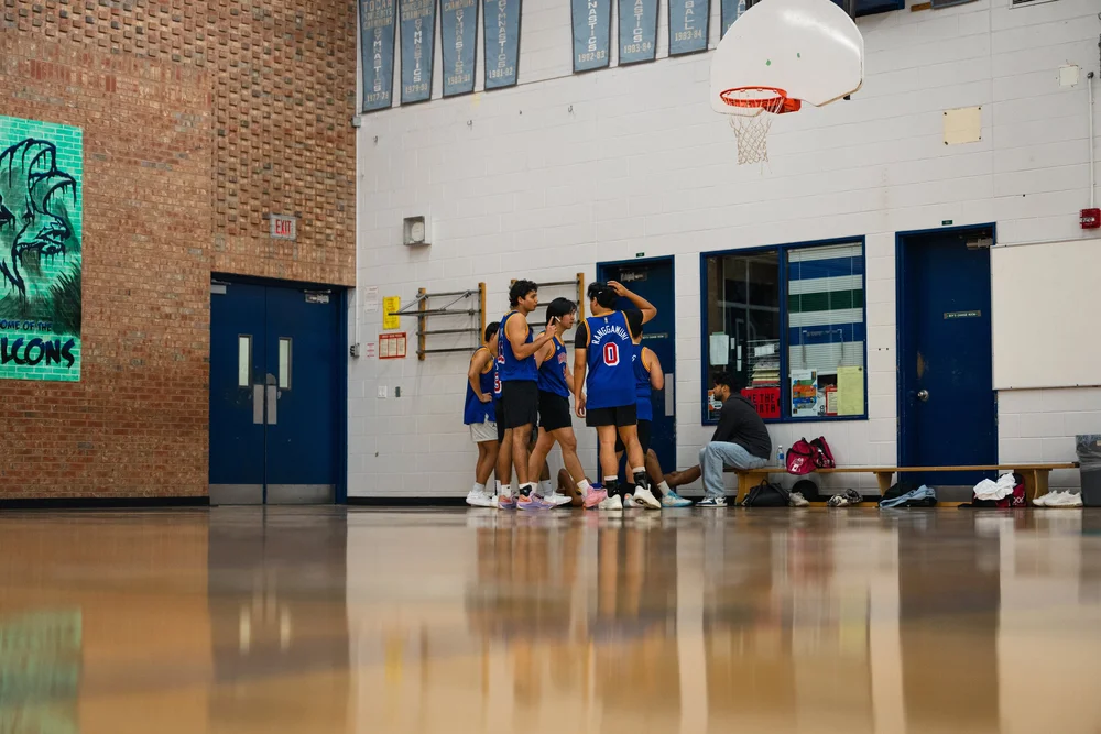Warriors players gather beside the bench in a wide view of the gym and reflective court.