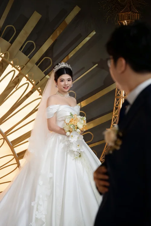 Woman holding a bouquet facing a man beneath a fan-shaped gold backdrop