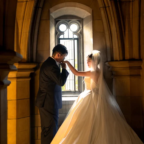 Man kissing a veiled woman’s hand beside a tall window