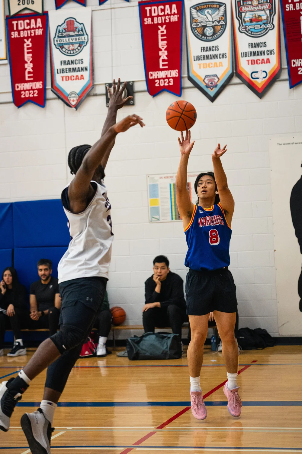 Warriors number 8 shoots as a white-shirted defender extends both arms.
