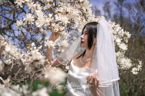 Veiled woman beside branches of white magnolia blossoms