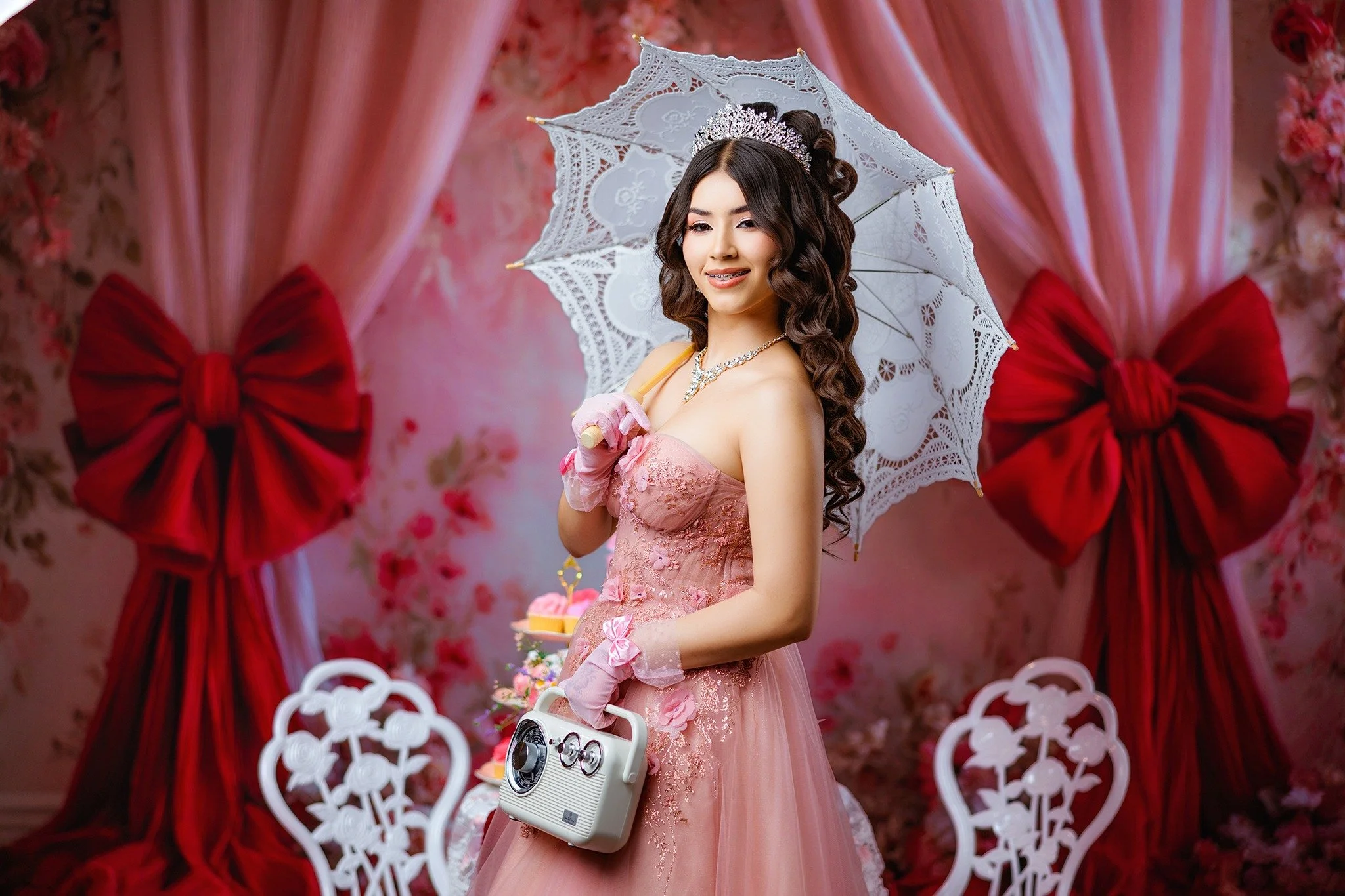 Quinceañera in a pink gown in a studio with pink curtains and red bows