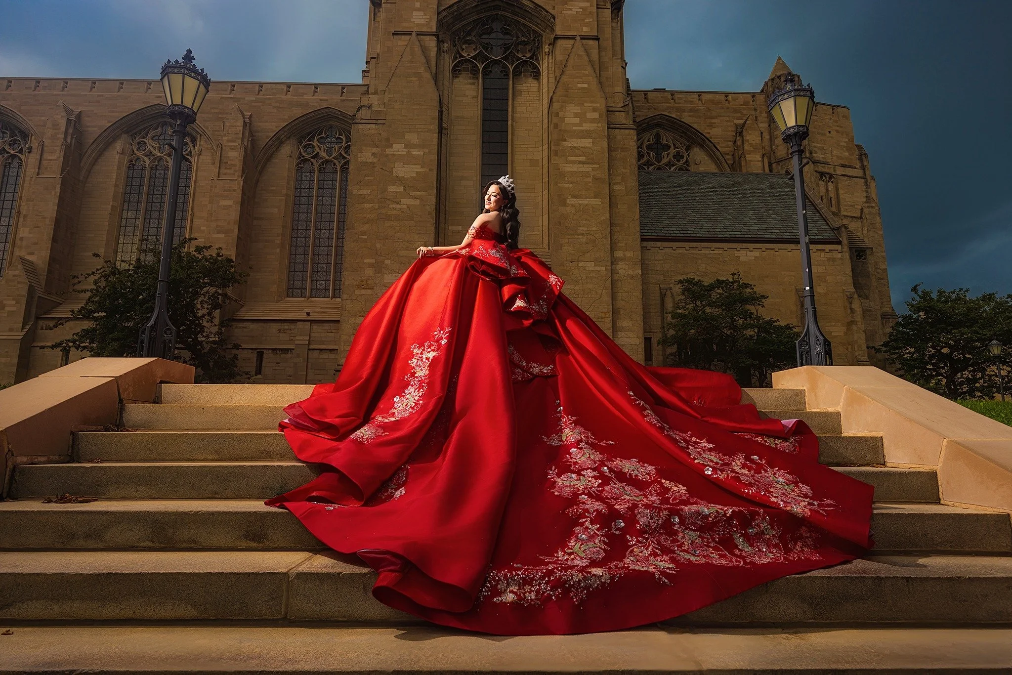 The long train of a red quinceañera gown sweeping across stone steps