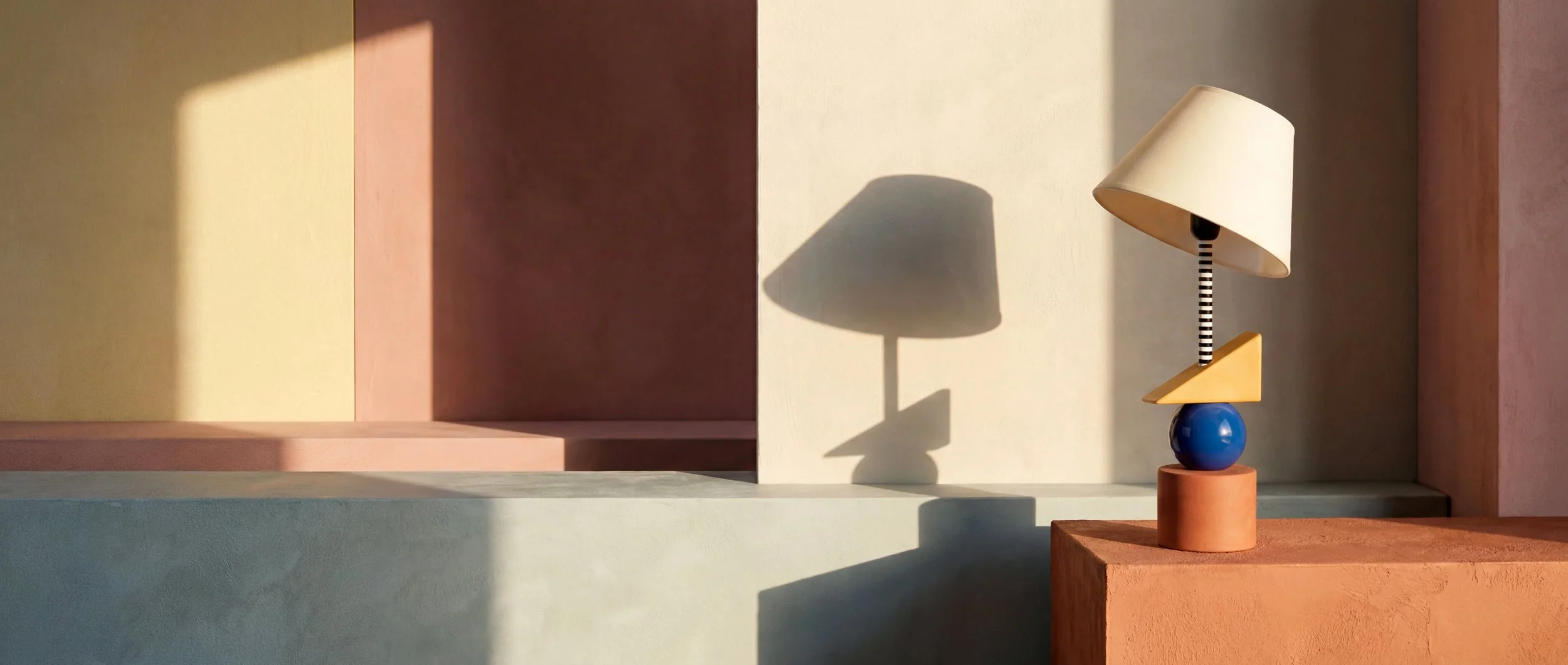 Lámpara y su sombra en una composición panorámica de arquitectura y luz cálida.