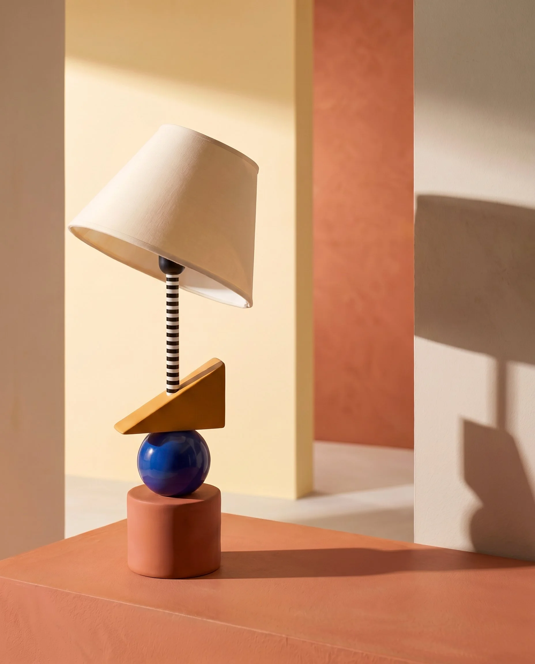 Lámpara de formas geométricas en una escena de luz cálida y planos arquitectónicos.