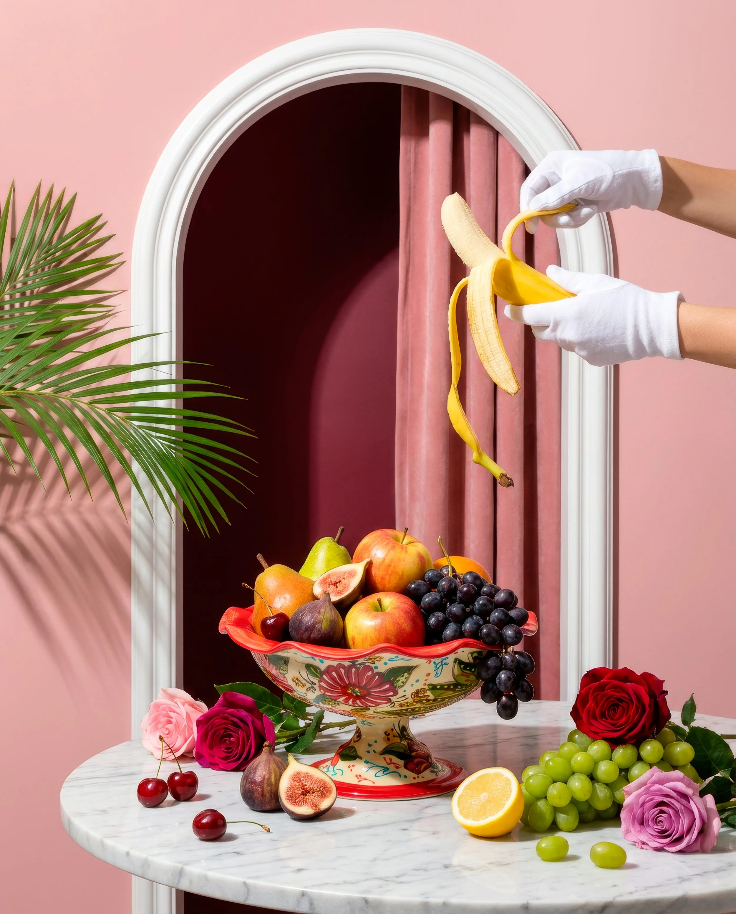 Frutero floral lleno de fruta junto a unas manos con guantes blancos pelando un plátano.